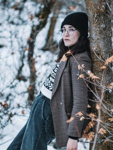 Frau lehnt am Baum im Schnee.
